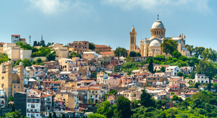 Blick über dicht bebaute Hügel in Algier mit auffälliger Basilika und grünen Hängen.