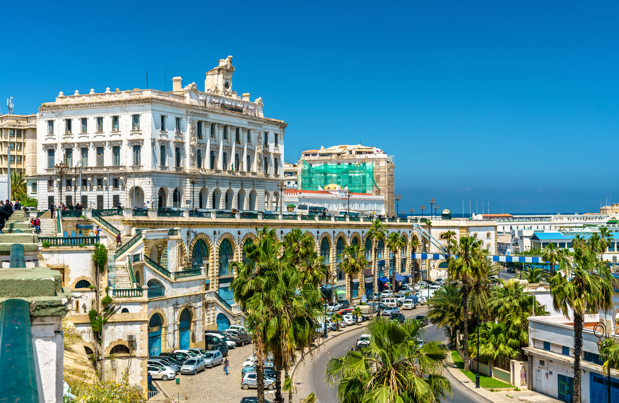 Uferstraße in Algier mit historischen Fassaden, Palmen und Blick Richtung Meer.