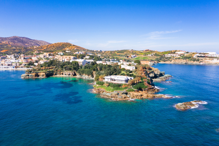 Luftaufnahme einer bergigen Halbinsel mit türkisfarbenen Buchten, weißen Gebäuden und üppigem Grün unter einem strahlend blauen Himmel.