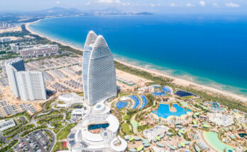 Ein gigantisches, segelförmiges Hotelgebäude aus Glas und Stahl thront über einer modernen Anlage mit zahlreichen Pools direkt am türkisfarbenen Meer.