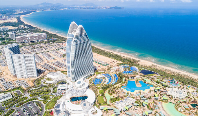 Ein gigantisches, segelförmiges Hotelgebäude aus Glas und Stahl thront über einer modernen Anlage mit zahlreichen Pools direkt am türkisfarbenen Meer.