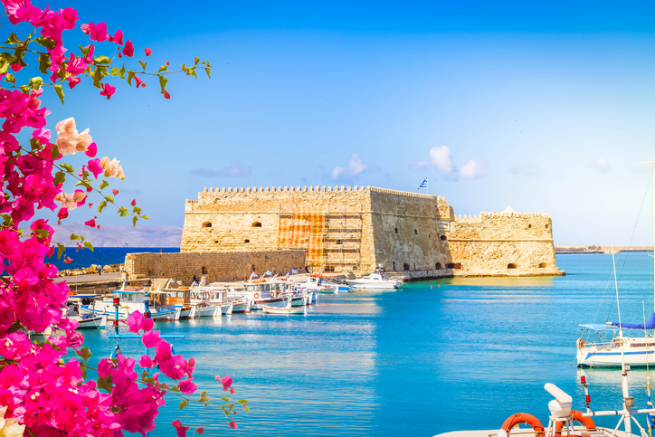Die massive Steinfestung Koules am alten Hafen von Heraklion, eingerahmt von leuchtend pinken Bougainvillea-Blüten und Fischerbooten im Vordergrund.