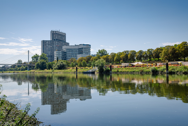 Blick über den ruhigen Neckar auf das markante Collini-Center und die Kurpfalzbrücke, die sich im Wasser spiegeln.
